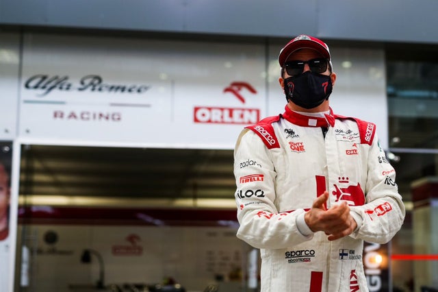 Kimi Raikkonen in his racing suit stading infront of Alfa Romeo garage