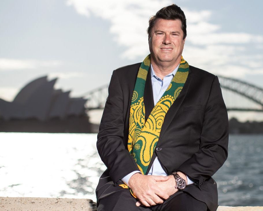Rugby Australia chair, Hamish McLennan seated in Sydney Harbour. The Sydney Harbour Bridge and Sydney Opera house are silhouettes in the background.