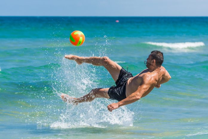 guy kicking ball at the beach