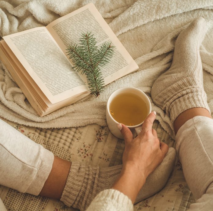 Cozy winter evening , warm woolen socks. Woman is lying feet up on white shaggy blanket and reading book. Cozy leisure scene Why your supplement routine may need a winter reset